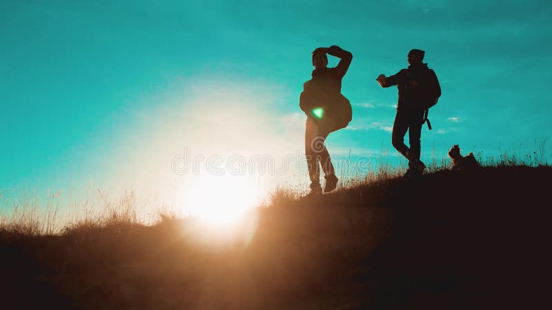 Teamwork, die Schwierigkeitssiegerfolg überwindt zwei Touristenschattenbild-Wanderermänner mit Rucksäcken bei Sonnenuntergang geh