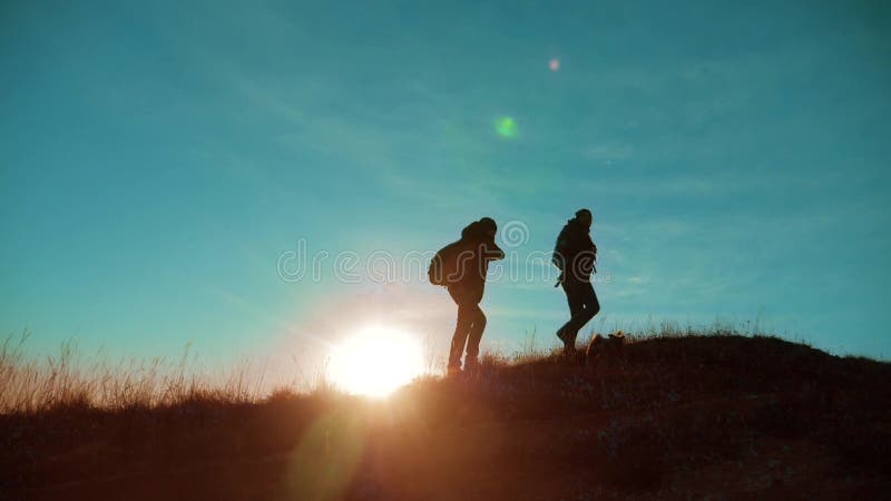 teamwork Zwei Wanderer, die Sonnenaufgang von der Spitze eines Berges und des Hundes genießen Zwei Wanderer mit den Rucksäcken, d