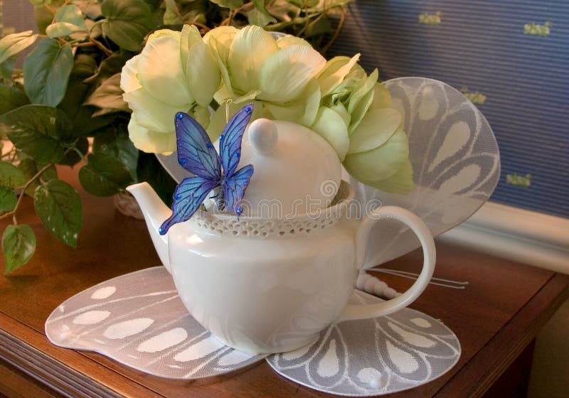 Teapot displayed decoratively on a butterfly mat with a blue butterfly attached t pot. Teapot displayed decoratively on a butterfly mat with a blue butterfly attached t pot