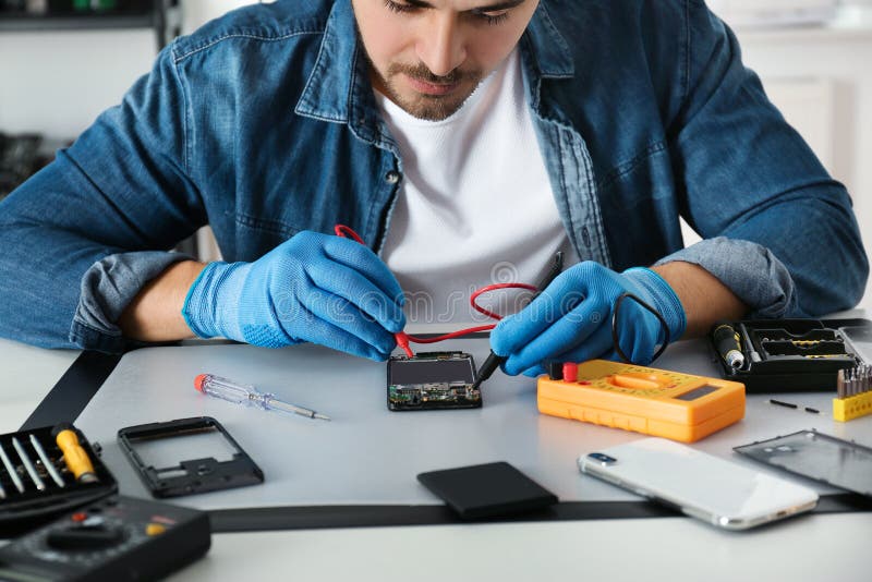 Technician Checking Broken Smartphone at Table in Repair Shop Stock