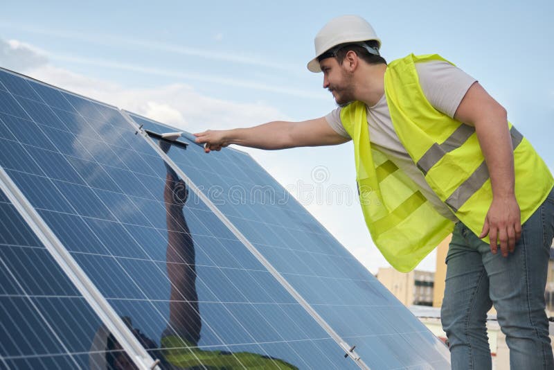 Technician Cleaning Solar Panels with a Squeegee Window Cleaner. Stock