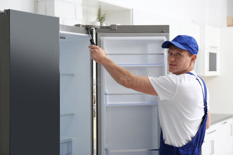 Technician with Screwdriver Repairing Refrigerator in Kitchen 库存照片 图片
