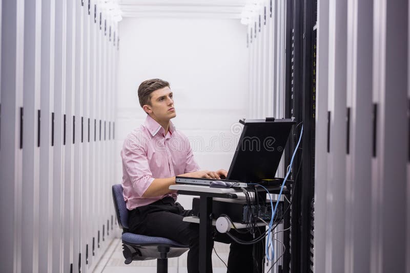 Technician sitting on swivel chair using laptop to diagnose servers in large data center
