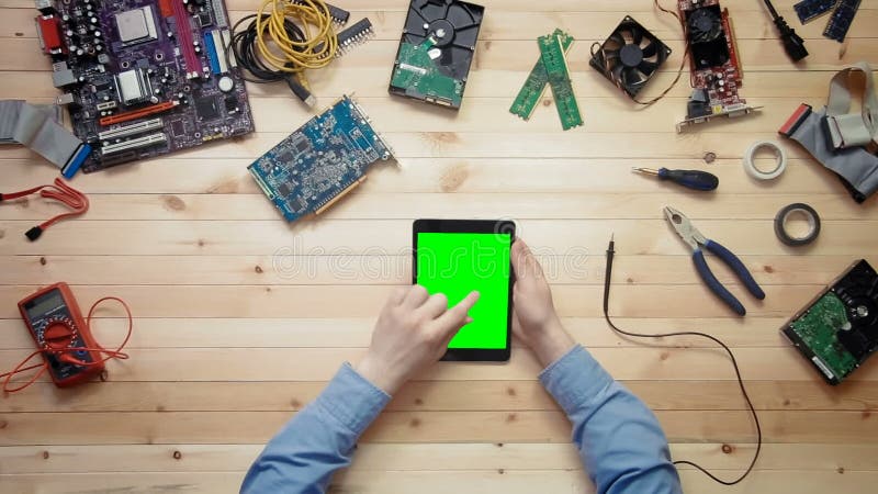 Technicien d'ordinateur de vue supérieure à l'aide du comprimé numérique avec l'écran vert au bureau en bois avec des outils et d banque de vidéos