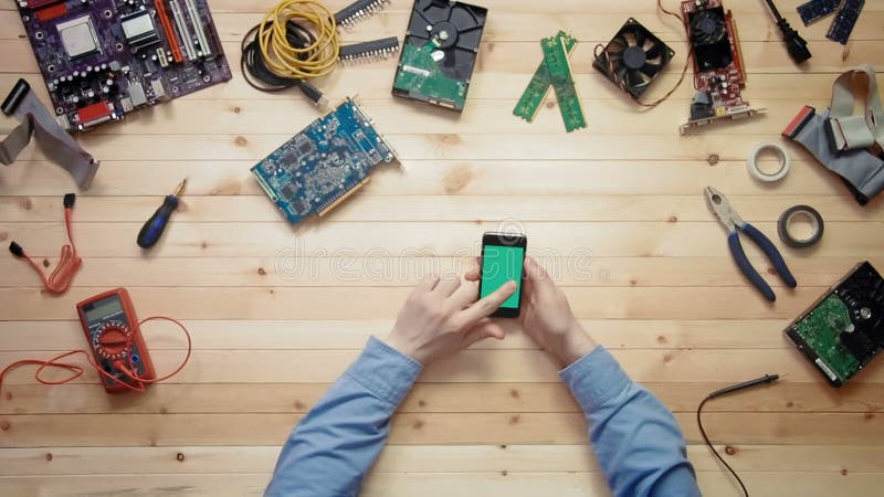 Technicien d'ordinateur de vue supérieure à l'aide du téléphone intelligent avec l'écran vert au bureau en bois avec des outils e clips vidéos