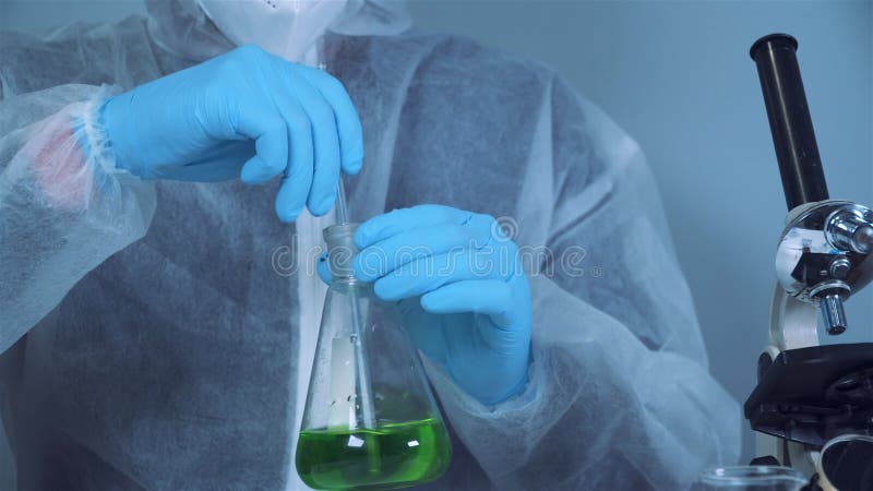 Technicien dans la main de vêtements de protection et d'agitation secouant le liquide dans le vert erlenmeyer en laboratoire chimi clips vidéos