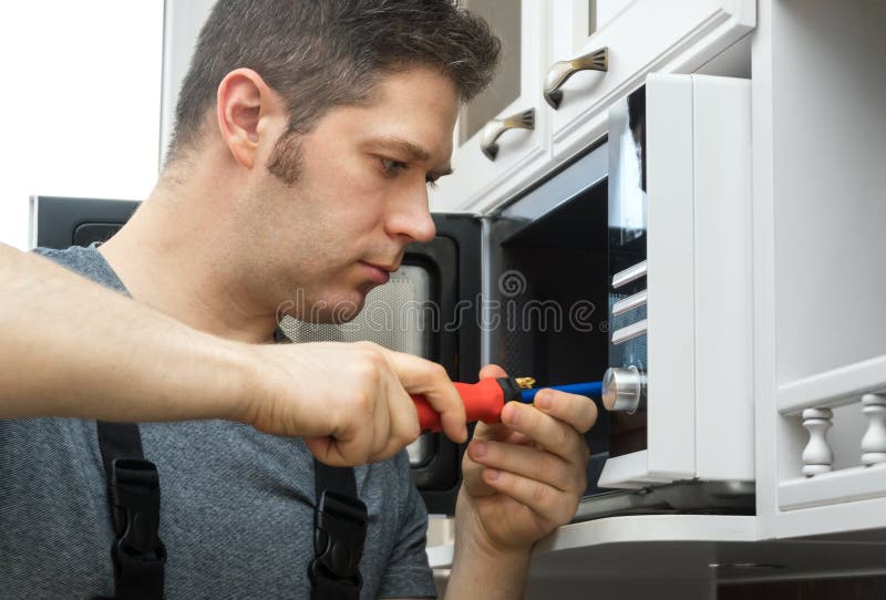 Technicien masculin réparant le four à micro-ondes image stock Technicien masculin réparant le four à micro-ondes image stock
