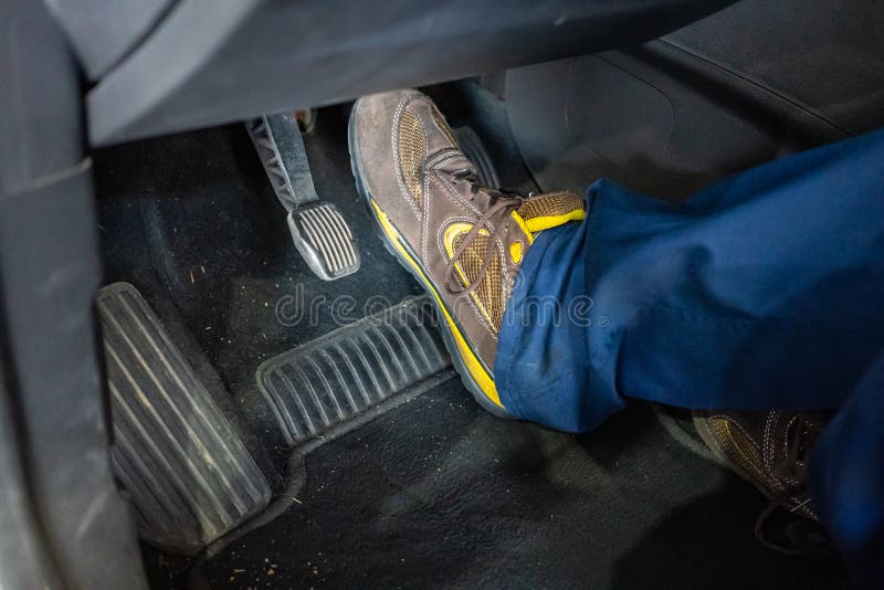 Technicien Ã©quipÃ© de bottes qui teste la pÃ©dale de frein d'une voiture lors d'une inspection du vÃ©hicule