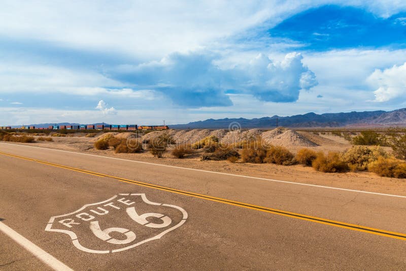 U.S. Route 66 highway, with sign on asphalt and a long train in the background, near amboy, california. Located in the mojave dessert. U.S. Route 66 highway, with sign on asphalt and a long train in the background, near amboy, california. Located in the mojave dessert