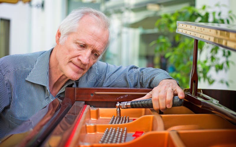 Tecnico anziano dello strumento di musica che sintonizza una tastiera di piano immagine stock Tecnico anziano dello strumento di musica che sintonizza una tastiera di piano immagine stock