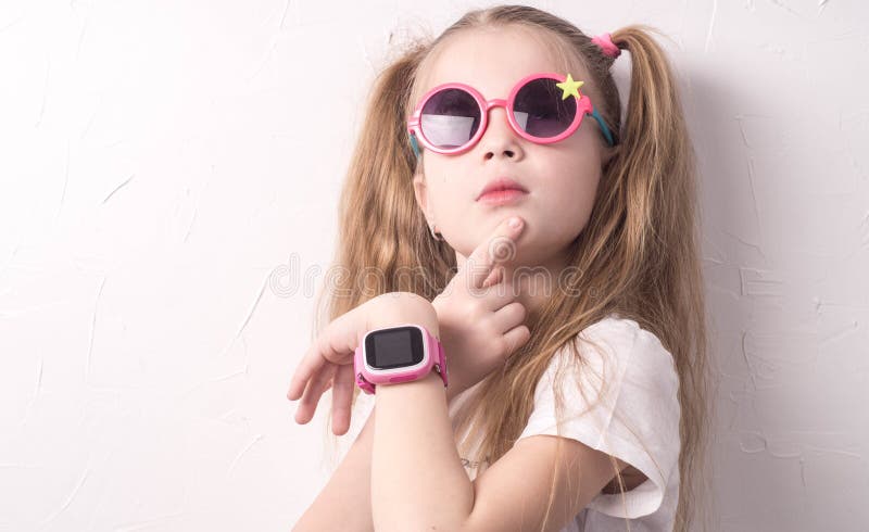 Tecnologia per i bambini: una ragazza che indossa i vetri rosa usa uno smartwatch immagini stock libere da diritti Tecnologia per i bambini: una ragazza che indossa i vetri rosa usa uno smartwatch immagini stock libere da diritti