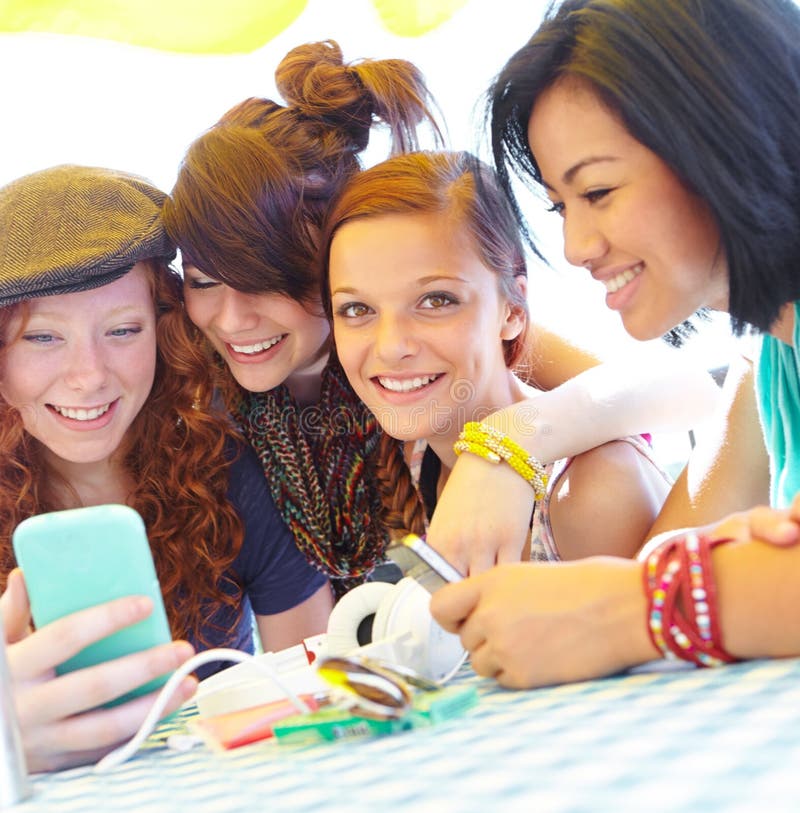 Teen technology. A group of adolescent girls laughing as they look at something on a smartphone screen. Teen technology. A group of adolescent girls laughing as they look at something on a smartphone screen