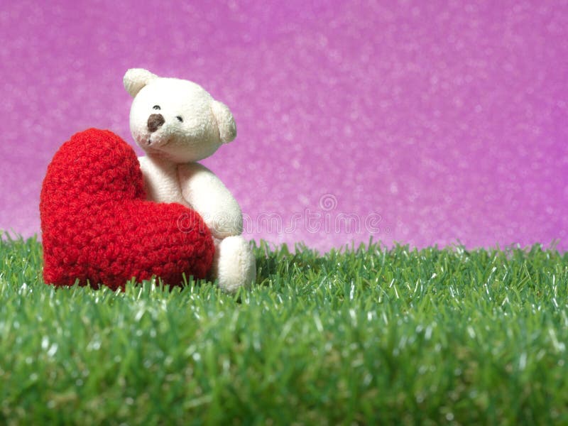 Teddy bear holding a handmade red heart on green grass background is royal pink.Copy space for text, Valentines day, love concept and love background.
