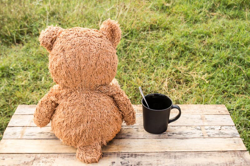 Teddy Bear Sitting Backwards and Coffee Cup on Wooden Table. Stock