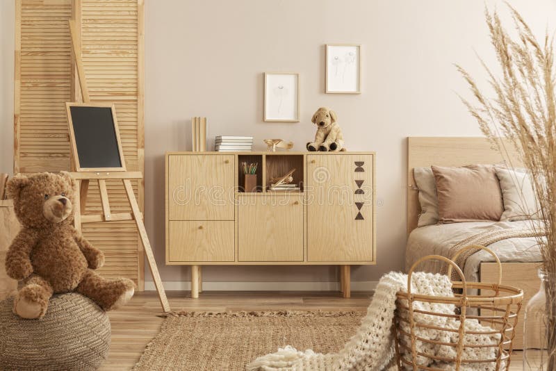Teddybeer op poef en klein bord op schildersezel in de modieuze slaapkamer van het jonge geitje met houten kabinet en beige bedde stock fotografie Teddybeer op poef en klein bord op schildersezel in de modieuze slaapkamer van het jonge geitje met houten kabinet en beige bedde stock fotografie