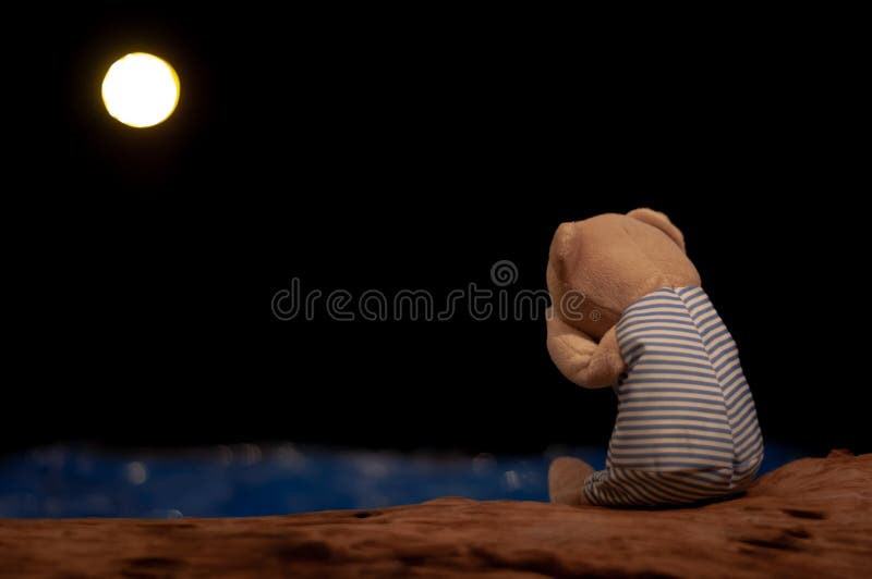 Teddybär, der allein gegenüberstellen zum blauen Meer und zum Mond schreit und sitzt