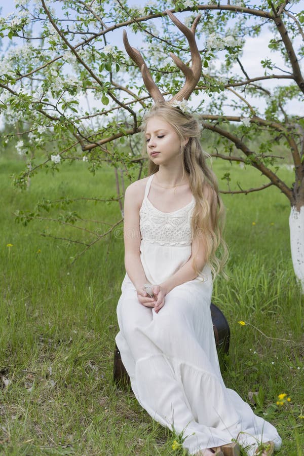 Teen beautiful blonde girl wearing white dress with deer horns o