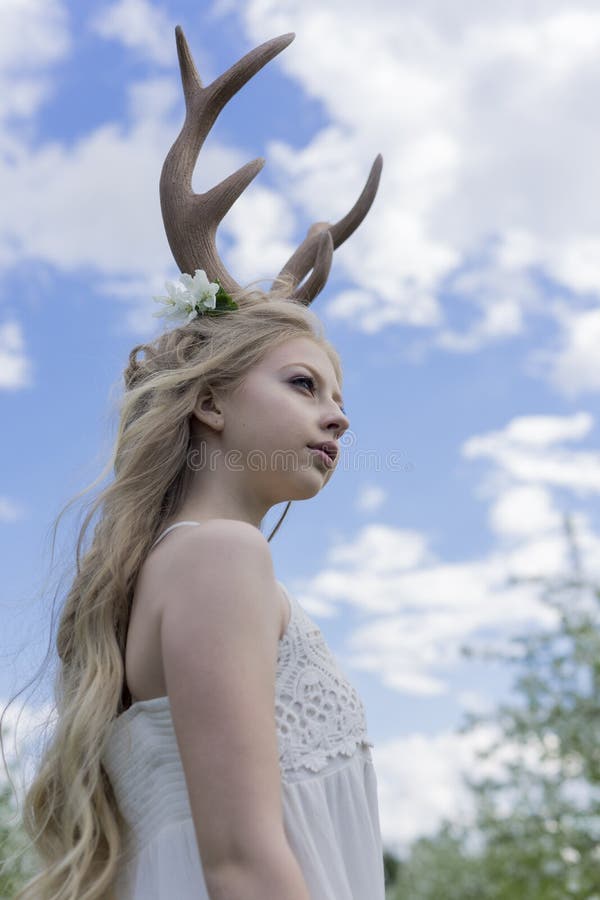 Teen beautiful blonde girl wearing white dress with deer horns o