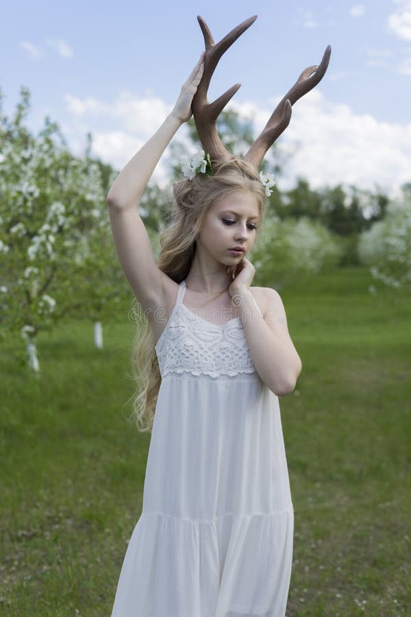 Teen beautiful blonde girl wearing white dress with deer horns o