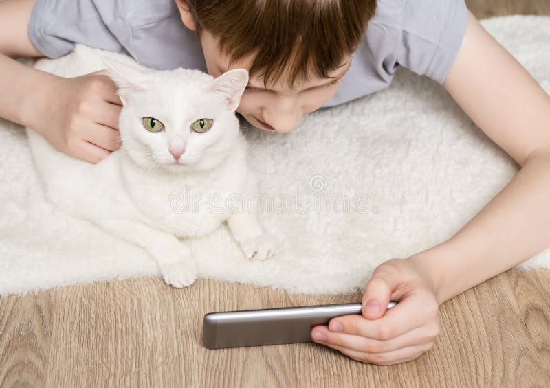 Teen boy and cat lying on carpet and watching video in smartphone