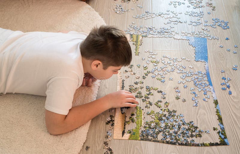 Teen boy collects a puzzle lying on carpet