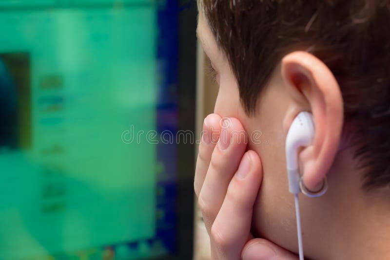 Image of a young teen, wearing earplugs, looking into a computer screen. Image of a young teen, wearing earplugs, looking into a computer screen