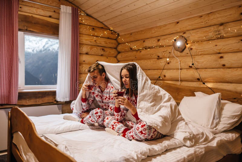 Teen friends in same Christmas pajamas relaxing in bed inside cozy log cabin with winter view