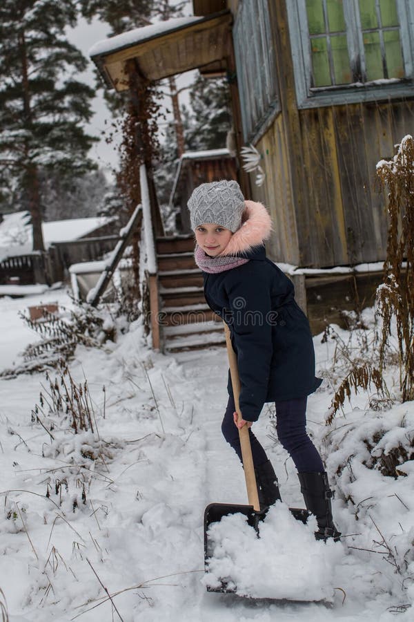 Teen girl cleans snow near a rural house. Winter. stock photo Teen girl cleans snow near a rural house. Winter. stock photo