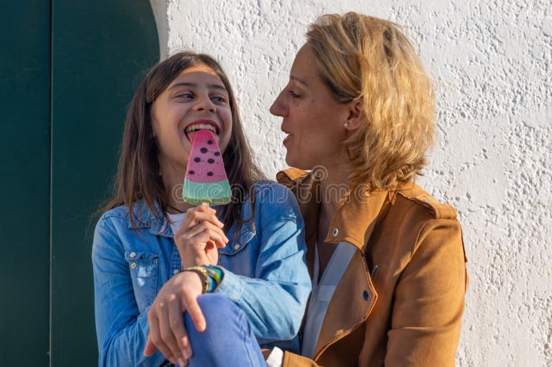 Teen girl eating a watermelon ice cream next to her mother in coastal town of Europe stock photography Teen girl eating a watermelon ice cream next to her mother in coastal town of Europe stock photography