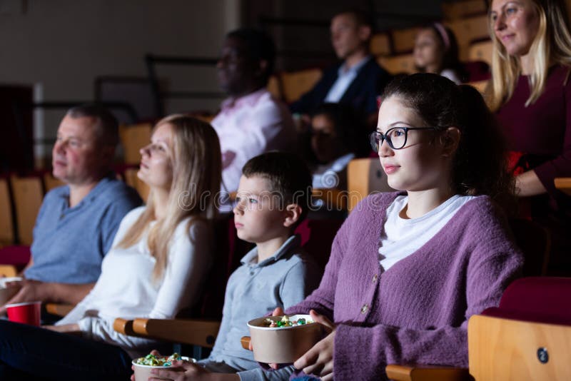 Teen girl with family watching film in movie theater. Portrait of teen girl with family sitting in movie theater with popcorn and drinks, watching interesting stock images