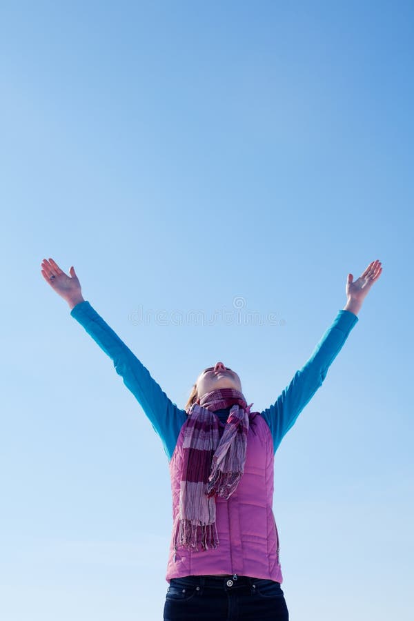 Teen girl staying with raised hands against blue sky