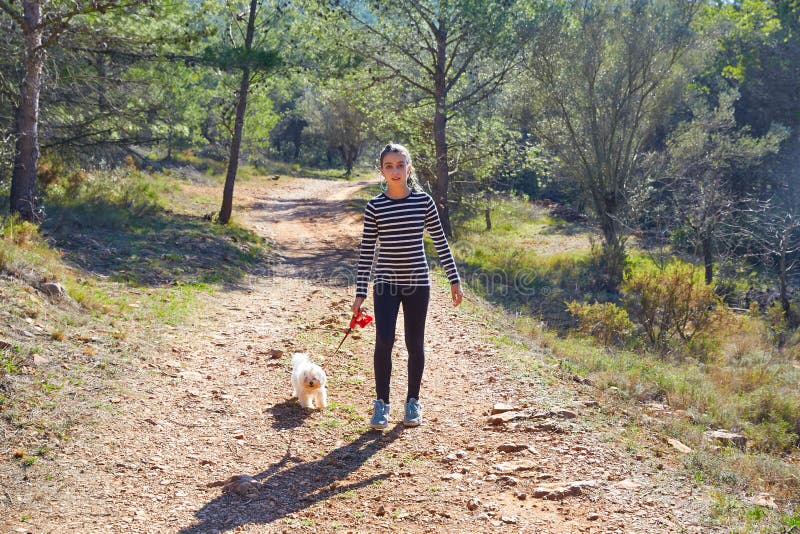 Teen girl walking with a white dog in forest
