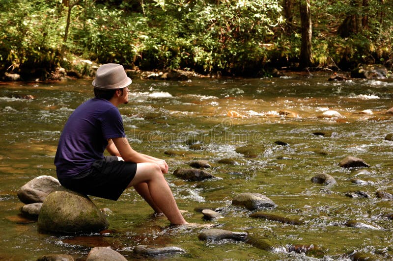 Teen sitting on river rocks