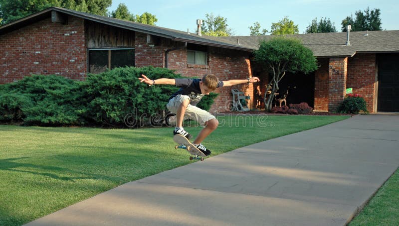 Adolescente chico través de el aire sobre su sobre el entrada de coches de suburbano.