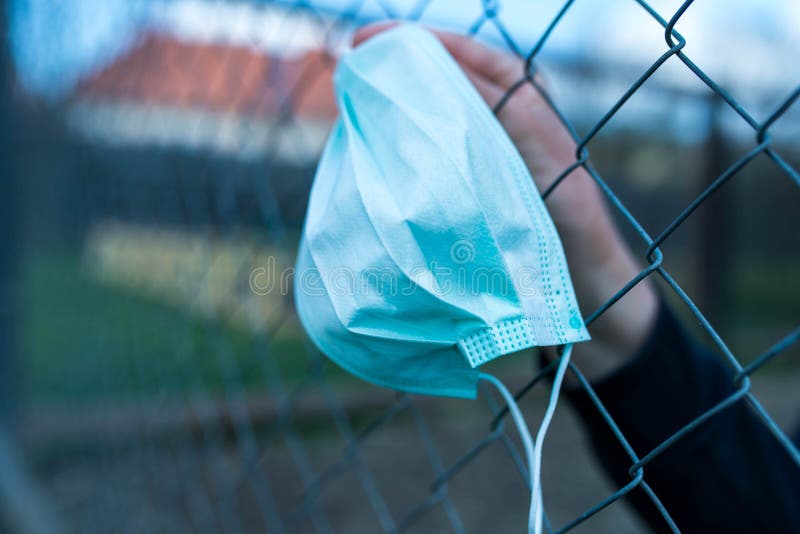 Teenage boy in isolation holding a medical mask trough the wired garden fence during the new Coronavirus pandemic.