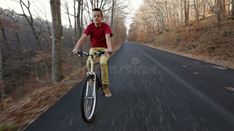 Teenage boy riding his bike on sunny autumn forest road downhill