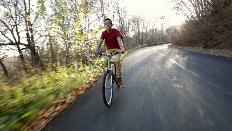 Teenage boy riding his bike on sunny autumn forest road downhill
