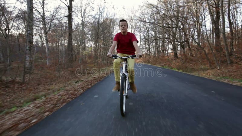 Teenage boy riding his bike on sunny autumn forest road - pedaling