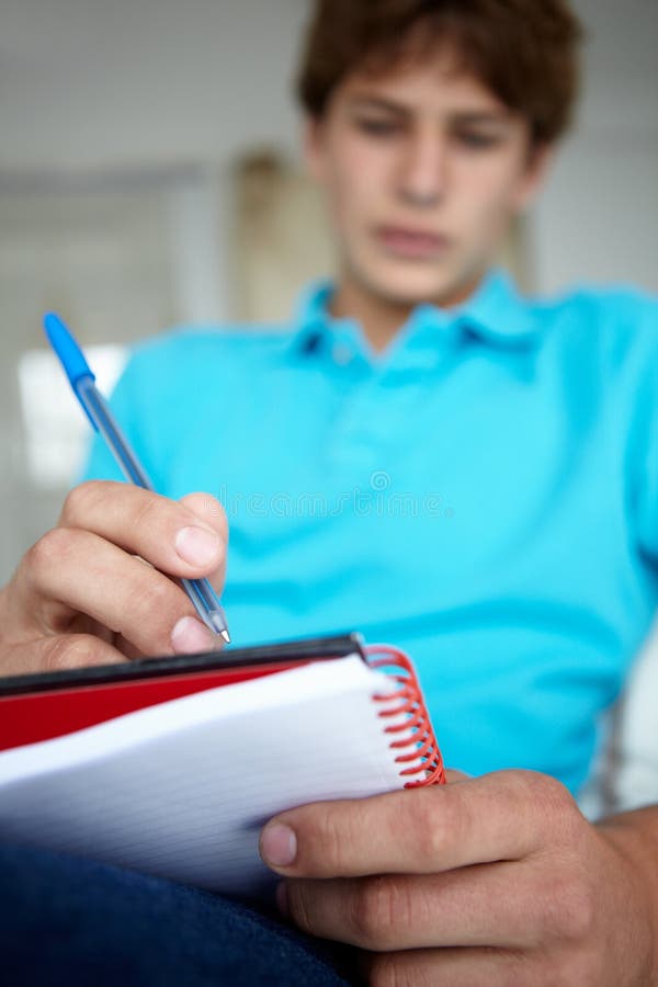 Teenage boy sat writing in notebook stock photo