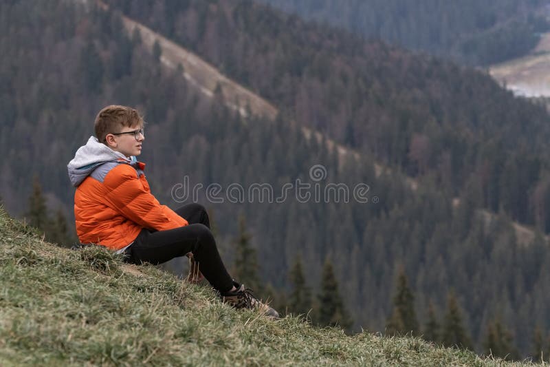 Teenage boy sits on hillside and looking at the distance, thinks about something. Weekend. Travelling with children
