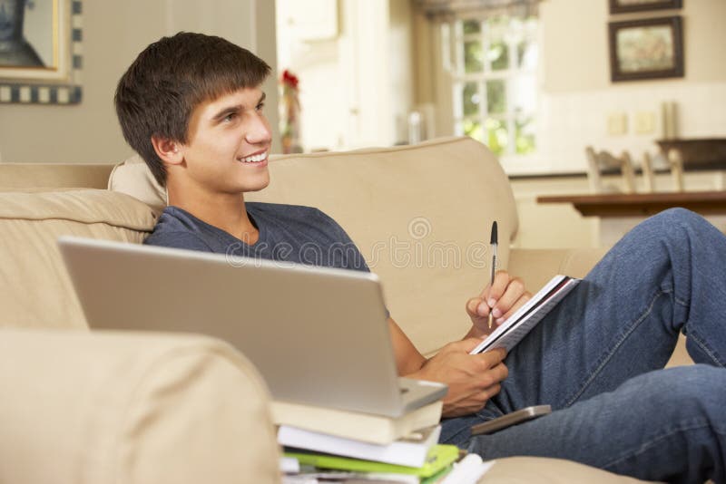 Teenage Boy Sitting On Sofa At Home Doing Homework Using ...