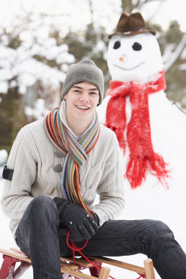 Teenage Boy With Sledge Next To Snowman