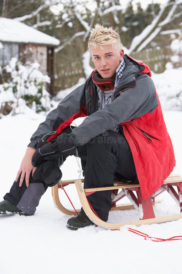 Teenage Boy With Sledge Next To Snowman