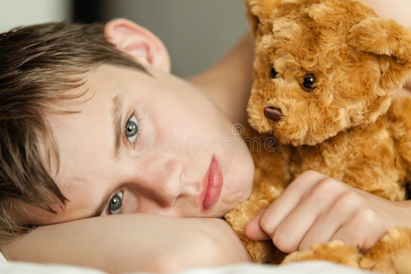 Teenage Boy Snuggling on Bed with Brown Teddy Bear