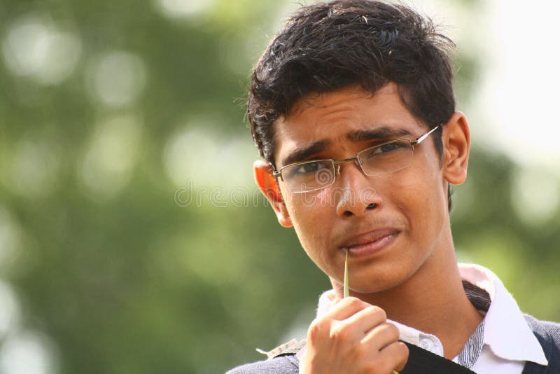 Teenage boy with specs biting grass blade