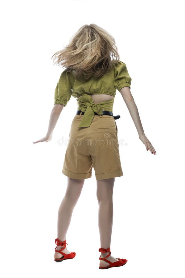 A teenage girl in beige shorts, a green blouse and red shoes is spinning with her hair flowing. Activity and positive. Isolated on