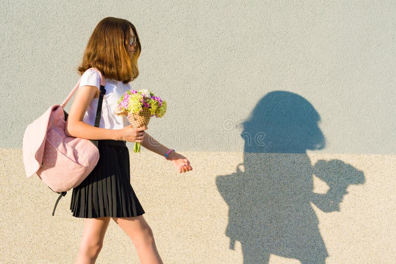 Teenage girl with bouquet, backpack. Goes against the gray wall, copy space. royalty free stock photo Teenage girl with bouquet, backpack. Goes against the gray wall, copy space. royalty free stock photo