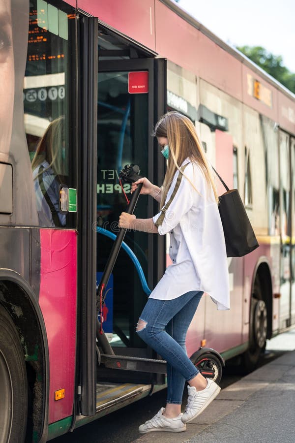 Teenage girl commuter entering city bus carring foldable electric urban scooter, wearing protective face mask against royalty free stock photos Teenage girl commuter entering city bus carring foldable electric urban scooter, wearing protective face mask against royalty free stock photos