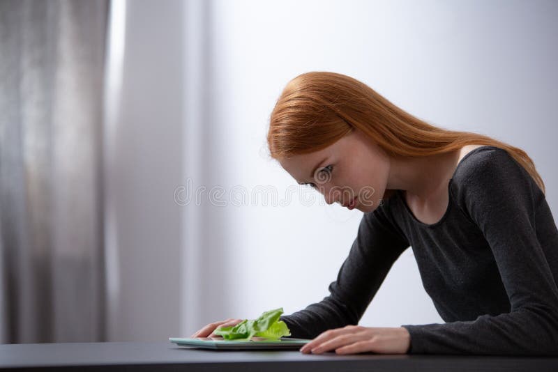 Teenage girl on diet sitting at table and looking at plate with lettuce