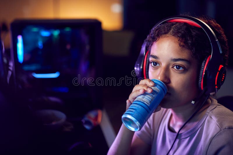 Teenage Girl Drinking Caffeine Energy Drink Gaming At Home Using Dual Computer Screens At Night